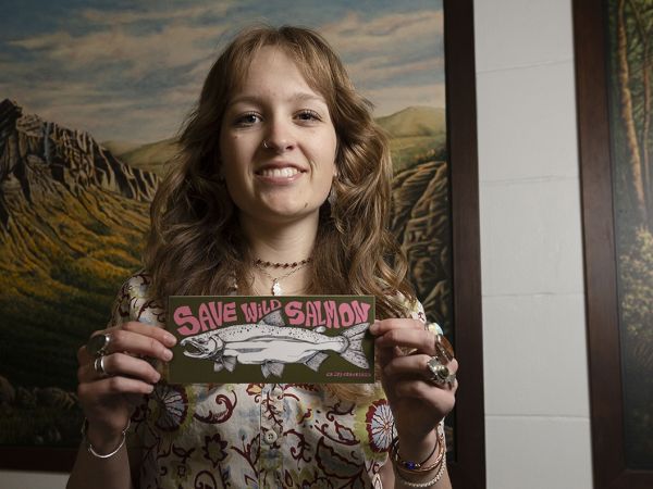 A picture of Ayla Kaltenecker holding a "Save Wild Salmon" sticker. a 