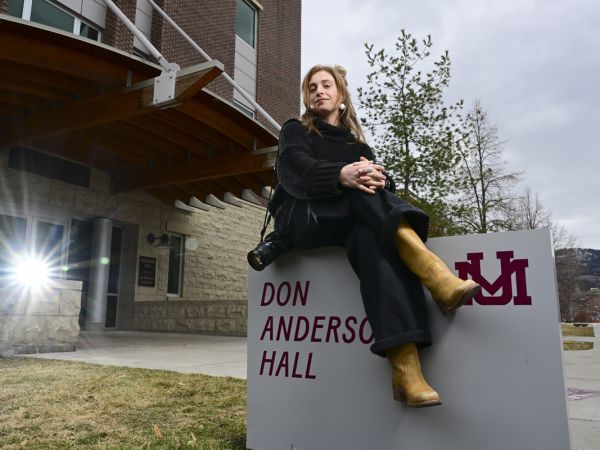 Recent UM journalism graduate Maddie McCuddy sits atop the building sign outside of Don Anderson Hall for a portrait photo.