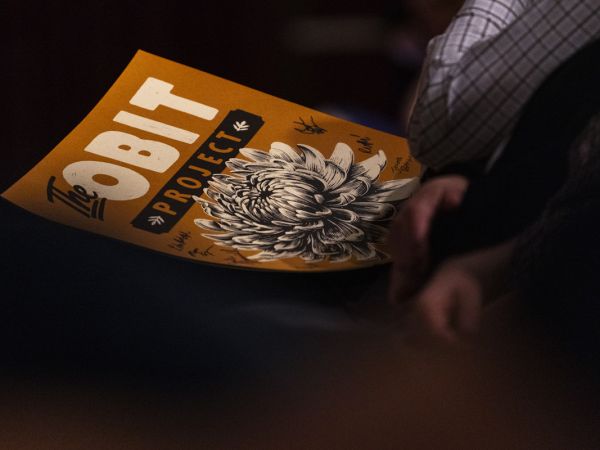 A signed copy of "The Obit Project" podcast's logo rests on an attendees lap.