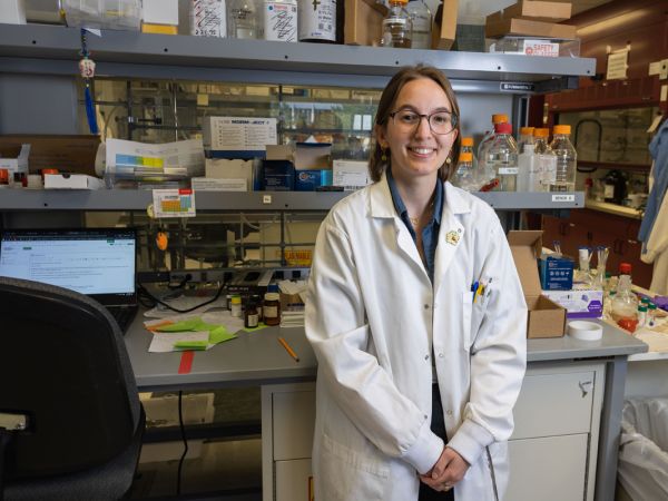 Annie Buchholz poses for a portrait photo in a lab setting while wearing a white lab coat.