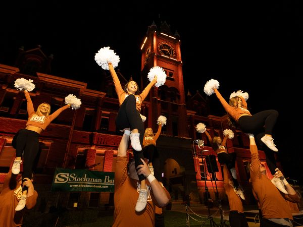 Cheerleaders cheer beneath Main Hall at night.