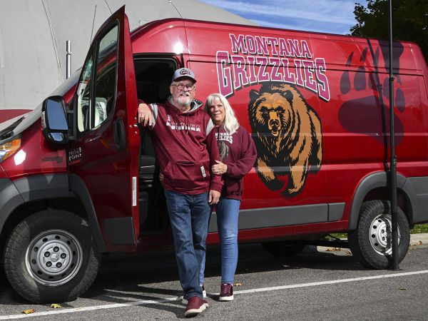 A picture of Brad and Carol Holm standing next to their Griz-decorated van.