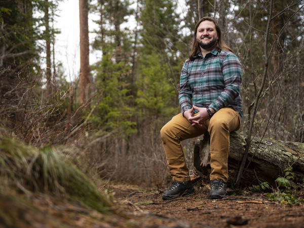 A UM student sits on a stump in the woods.