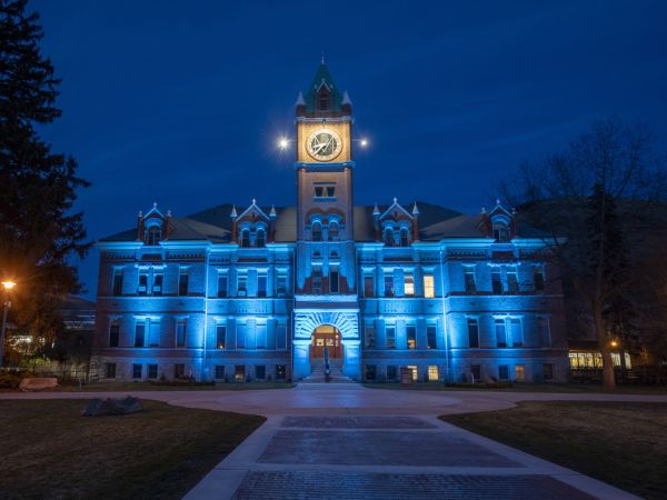 A view from the University of Montana Oval of Main Hall lit up in teal at night