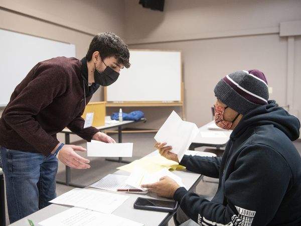 A UM student hands a paper across a table to a member of the public.
