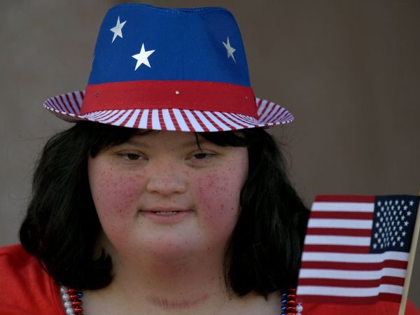 Woman with Down syndrome waving an American flag and wearing a hat with stars and stripes