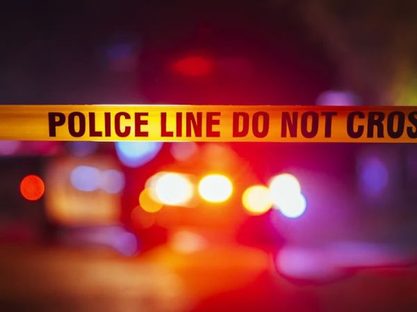 Police Line tape with flashing police car lights in background.