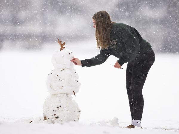 Snow man with girl putting a leaf on it