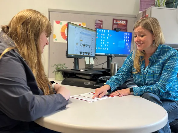 A UM Student and an Experiential Learning and Career Success Coach meet, sitting down in a office with a table in between them revieing a resume.