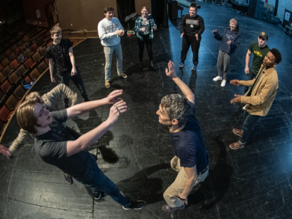 A circle of students onstage playing a physical game
