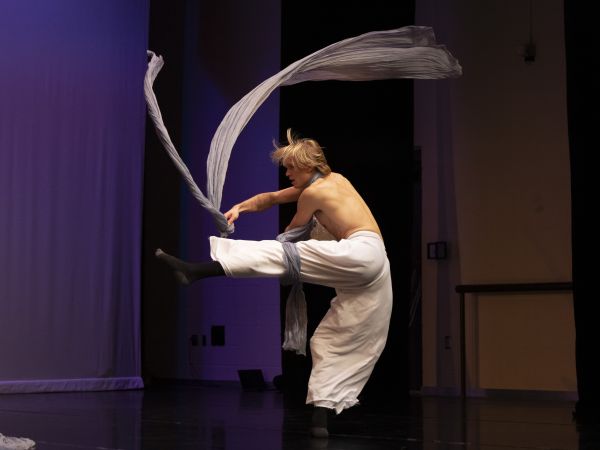 A man dancing on stage with a long piece of fabric
