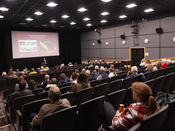People seated in a theater listening to a man speak