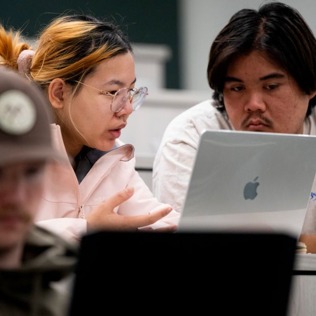 two students looking at a laptop, the girl is talking
