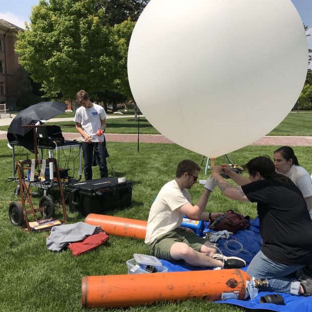 people on a field performing various activities, some holding a weather balloon and other gathered around instruments