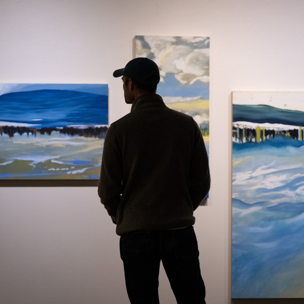 A lone figure stands in front of a UC Gallery wall with art displayed