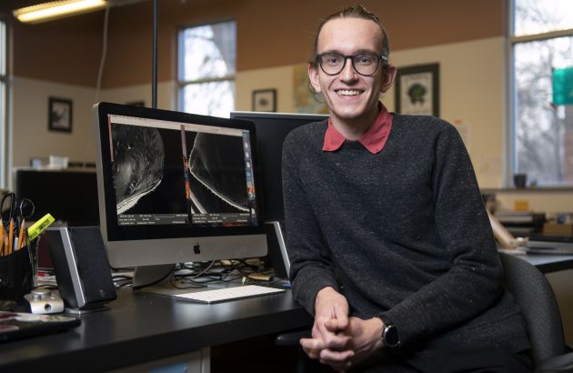 UM senior Devin Hunt turns away from a desktop computer and smiles at the camera