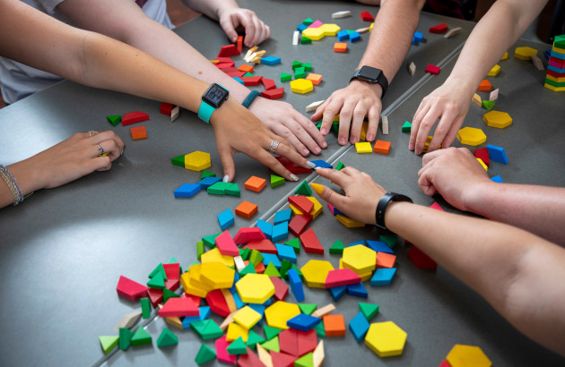 Several hands reaching for colored blocks on a table