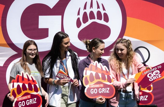 students holding up grizzly bear paw print signs that say "I decided to Go Griz"