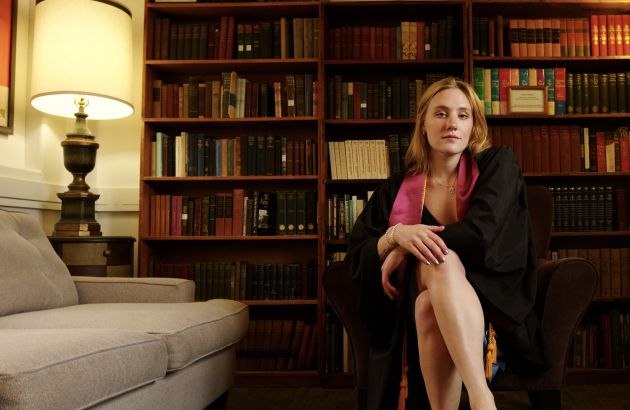 dylan yonce posing in graduation regalia in front of book shelf