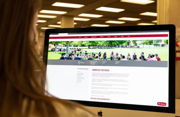 Laptop screen displays UM web with directions on completing a FAFSA