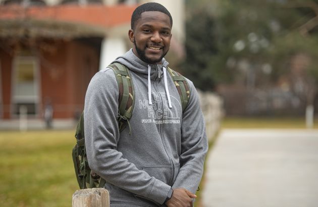 UM senior TraJon Cotton leans against a fence and smiles at the camera while wearing a backpack.