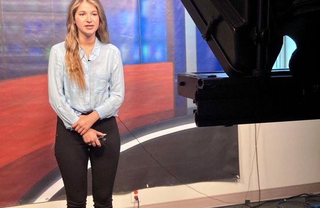 Woman with brown hair looking at camera in TV studio.