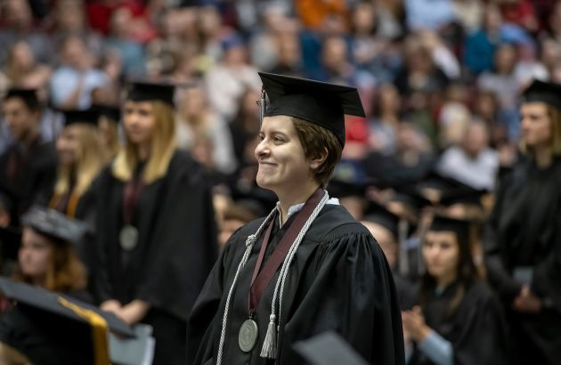 A graduate wearing a cap and gown stands during UM's fall Commencement ceremony