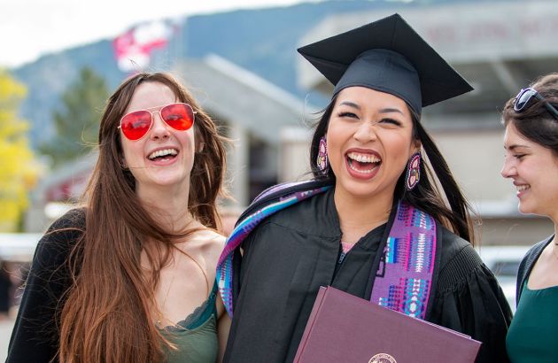 A graduating student smiles as she embraces friends in a side-hug