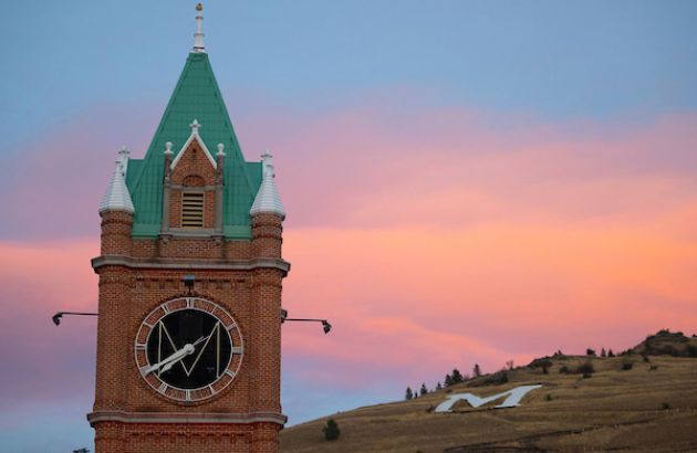 The clock tower of Main Hall at UM with Mount Sentinel in the background and a pink cloud in the sky