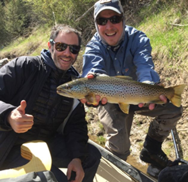 Two men holding up a brown trout while fly fishing.