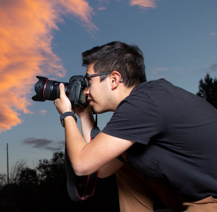 Man points camera with pink sky in background.