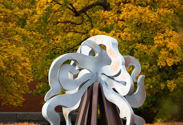 metal art work piece displayed in front of autumn trees of yellow and green