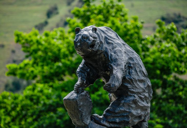 Griz bear statue near the oval on campus with green trees in the background