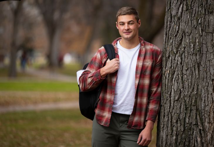 UM student standing next to tree on UM campus holding backpack