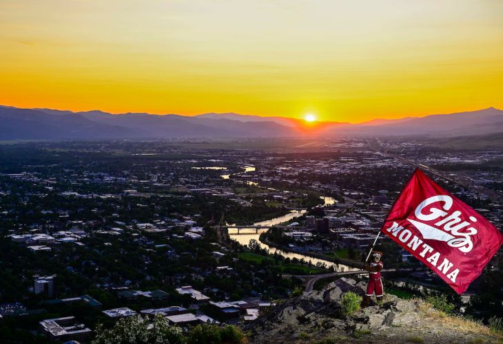 Monte on Mountain waving UM grizzly sign with sunset in background