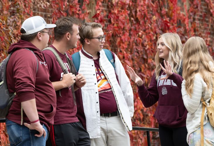 UM students chatting in a group outside of ivy covered building