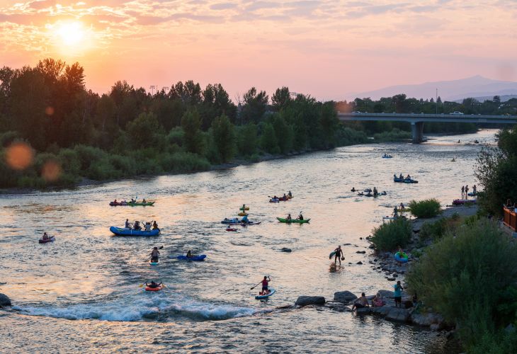 Many people kayaking, paddleboarding, and floating on the Clark Fork river at sunset in Missoula