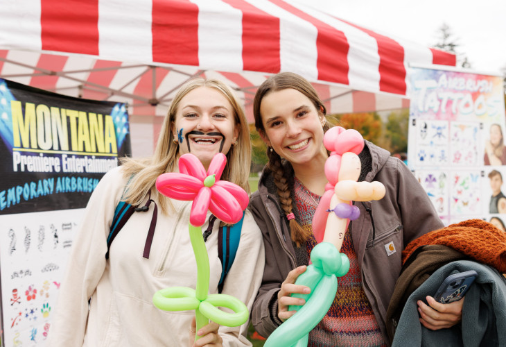 Two girls smiling holding blown up balloons 