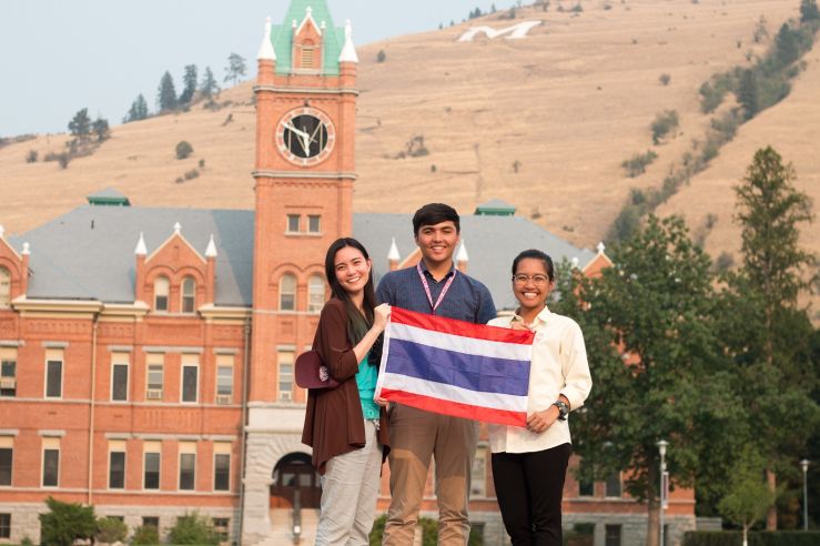 students posing at UM with the flag of Thailand