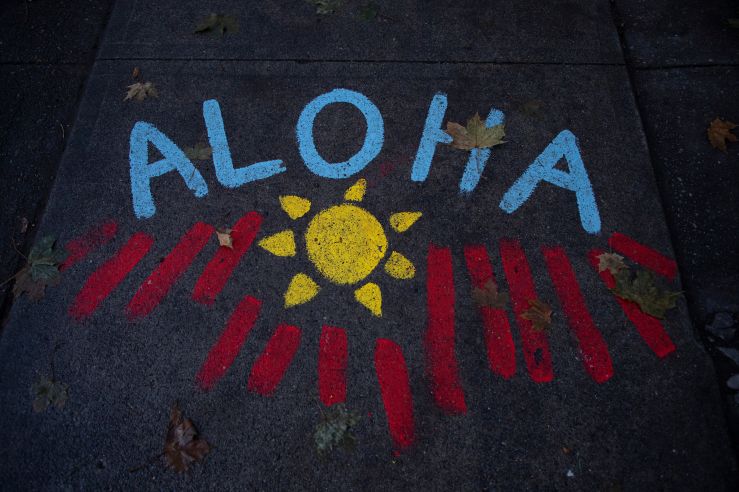 The word "Aloha" is painted with a sun on a sidewalk