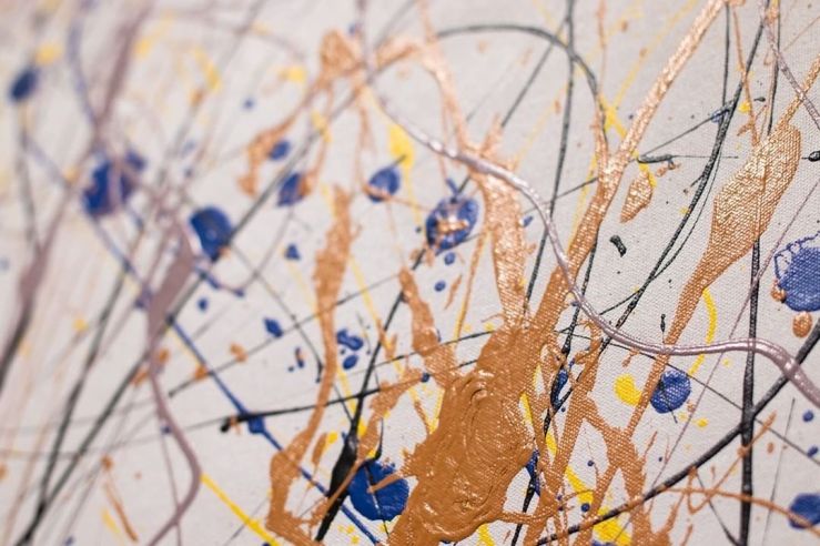 closeup of abstract drip painting in gold and deep blue on white with splashes of yellow and lavender