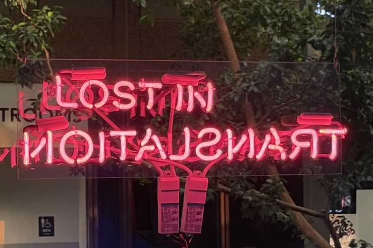 pink neon sign reading lost in translation in gallery window, with garden trees in background