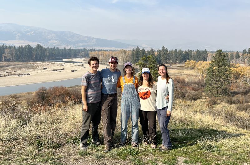 Five biologists smile at the camera with a vista of mountains and the Bitterroot River behind them.