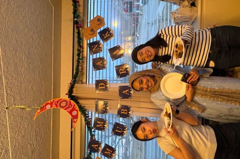 3 Students posing for a photo under a "Ramadan Mubarak" banner