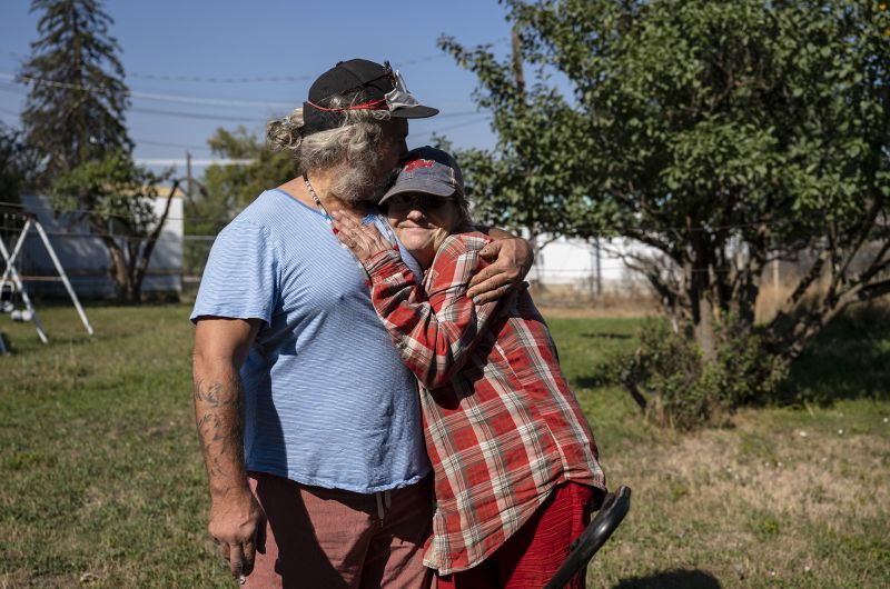 Man in blue shirt hugs woman in plaid shirt.