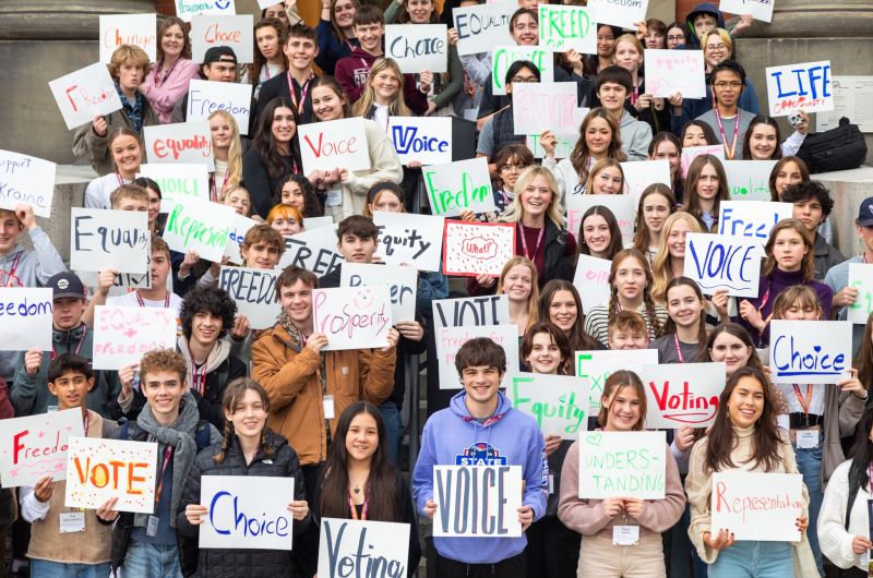 A group of highschool students smiling holding signs