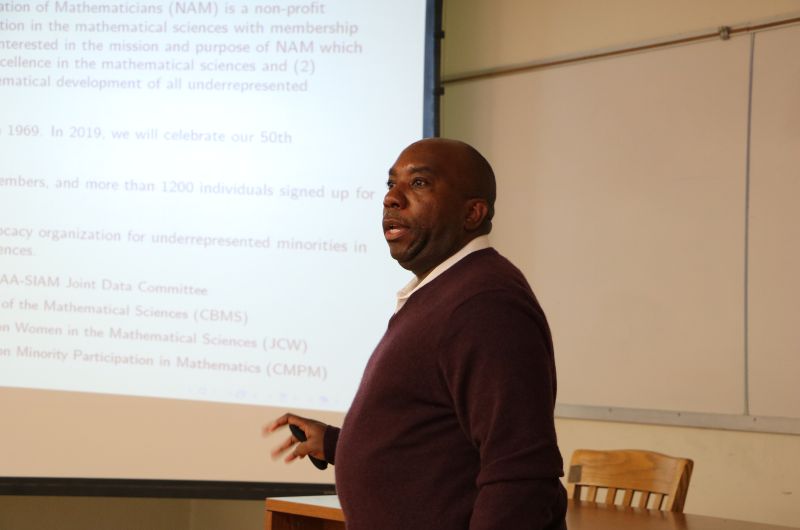 Edray Goins talks in front of projector screen 