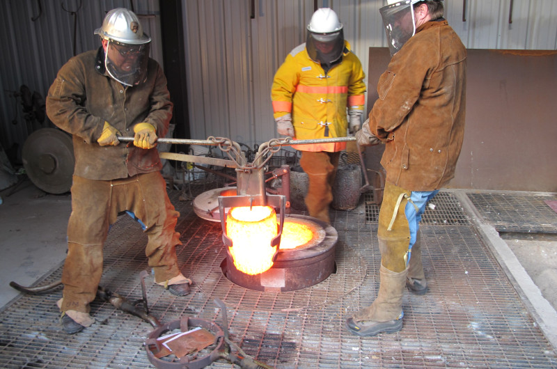 Brad Allen and Brad Evanger, of Facilities Services, lift the crucible while technician Patrick Eckman watches.