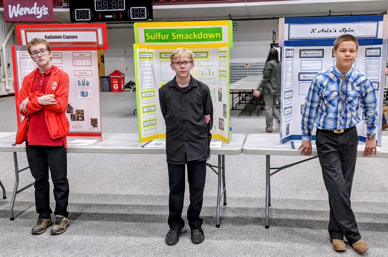 3 kids standing in front of boards