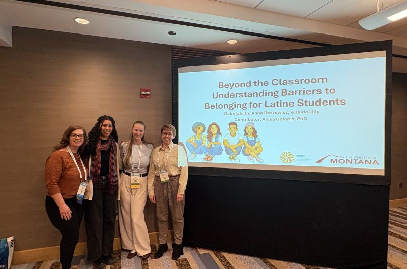 Three graduate students and a professor standing in front of a conference presentation screen